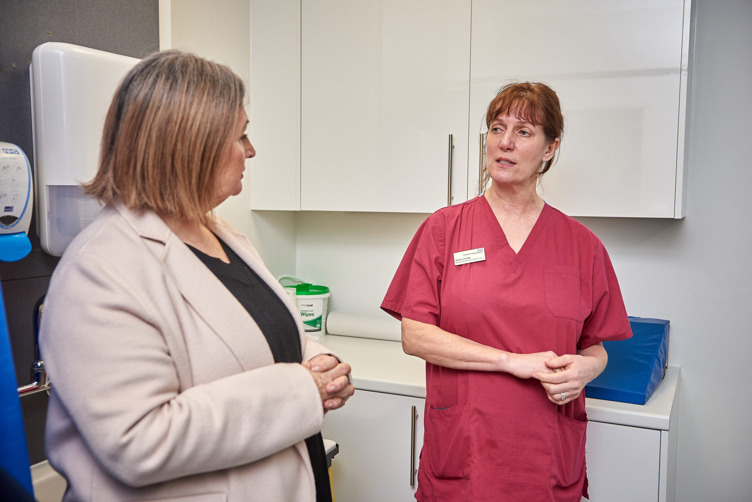 Two people talking, one is wearing red scrubs.