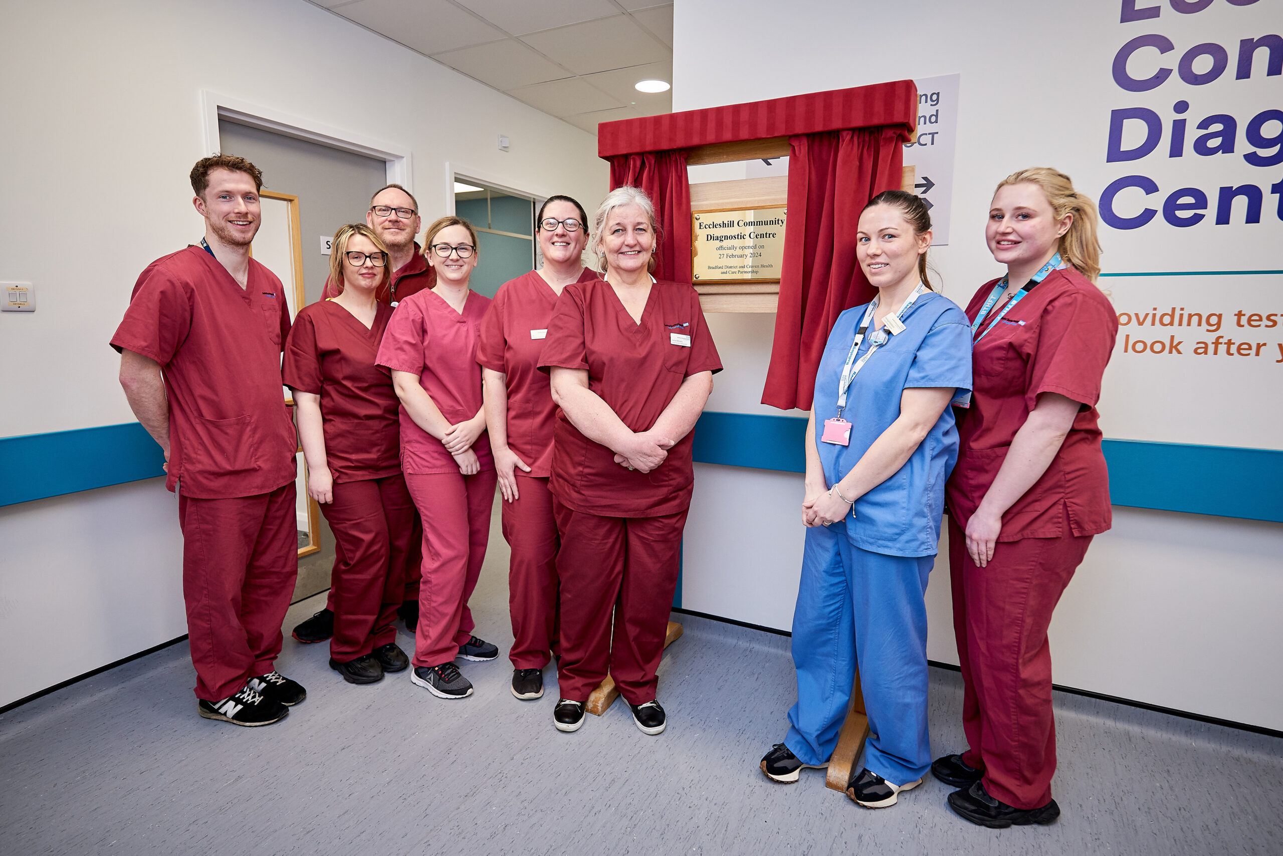 Picture of eight people in scrubs. Standing in front of a plaque.
