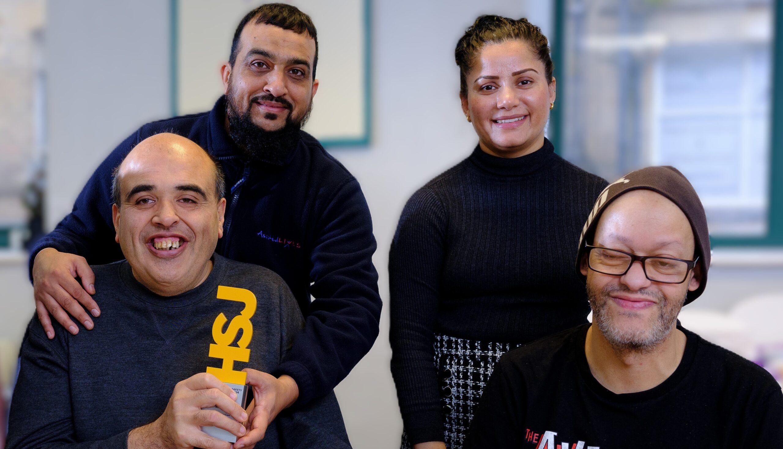 This image shows 4 people all smiling. One person is holding a yellow award.