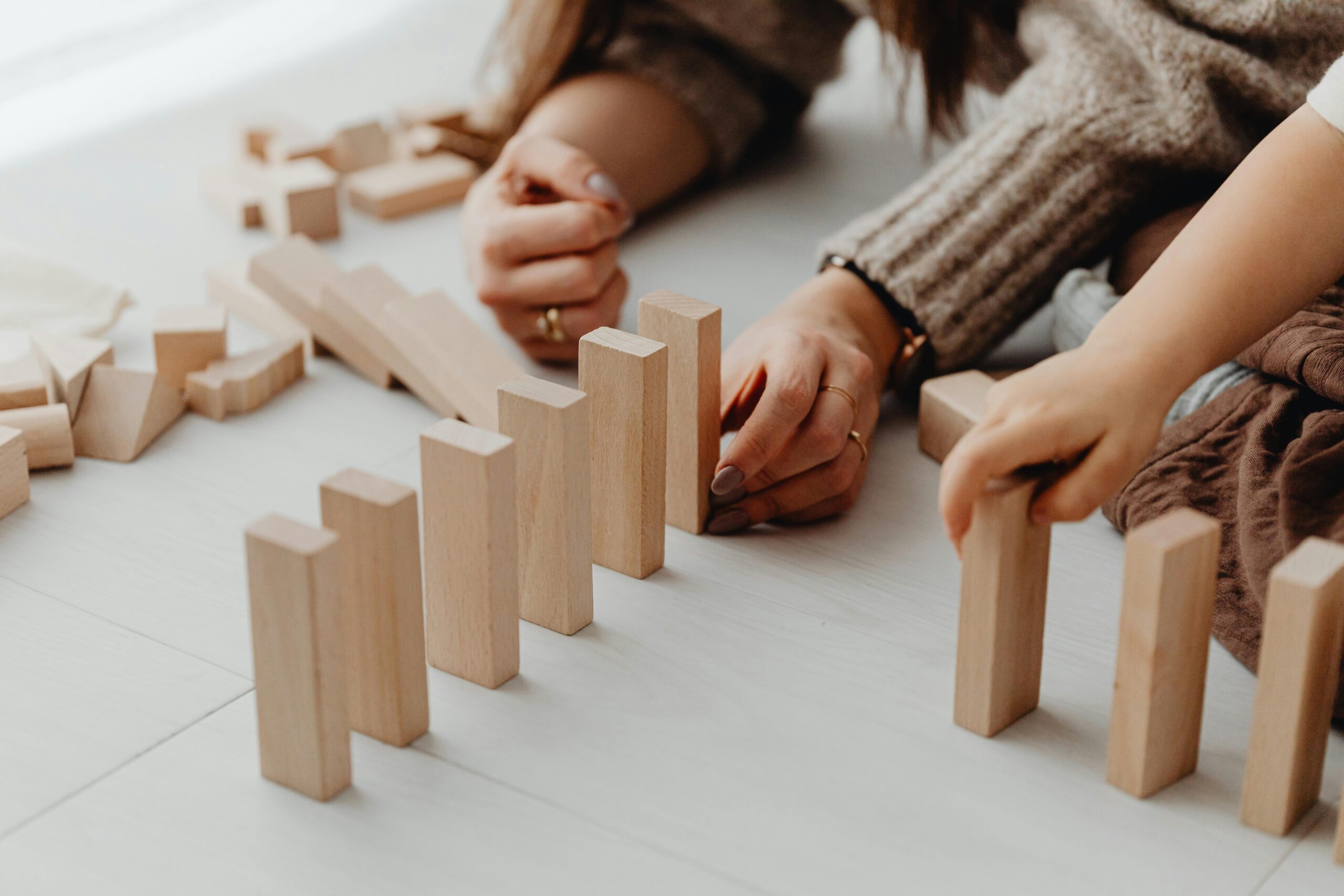 The picture shows a woman and a child playing with wooden blocks on the floor