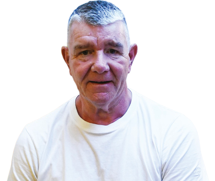 Man with short grey hair, wearing a plain white t-shirt, looking at the camera against a light background.