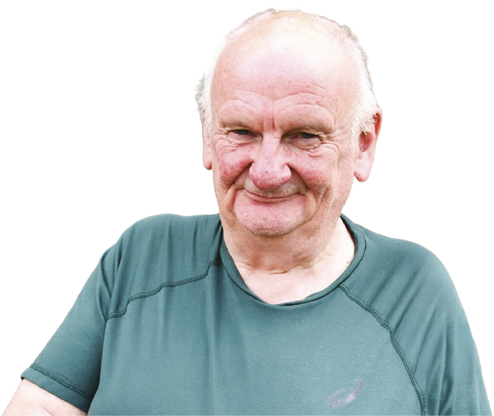 Older man with a kind smile, wearing a green T-shirt, looking at the camera against a neutral background.