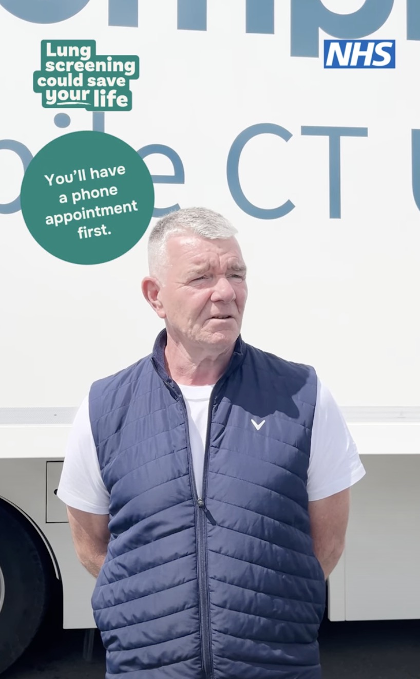 A man standing outside an NHS mobile CT unit with campaign text that reads: ‘Lung screening could save your life’ and ‘You’ll have a phone appointment first.