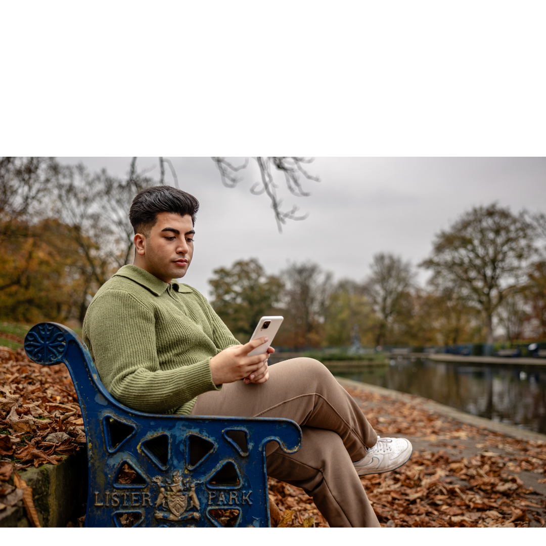 A young man sat on his phone on a bench